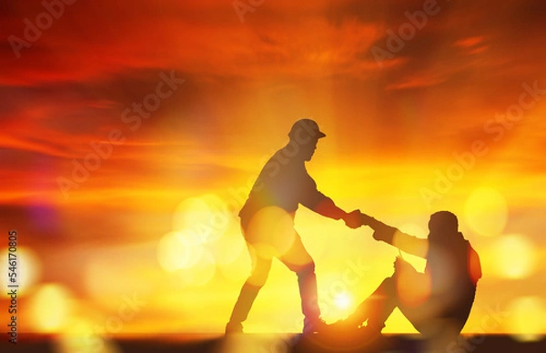 Fototapeta Silhouette engineer and male foreman pulling handshake, pulling the hand of a male worker who sits in despair, wanting to have a spirit of hope and stand up for success : Sunset background