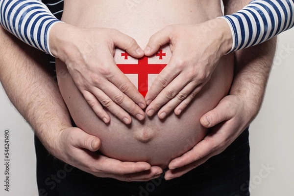 Fototapeta Georgian family concept. Man embracing pregnant woman belly and heart with flag of Georgia colors closeup