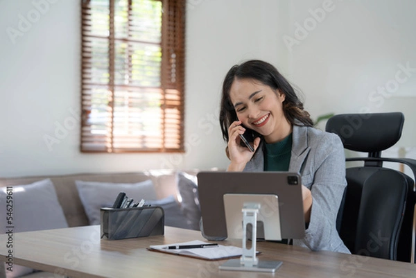 Fototapeta Smiling beautiful Asian businesswoman analyzing chart and graph showing changes on the market and holding smartphone at office.