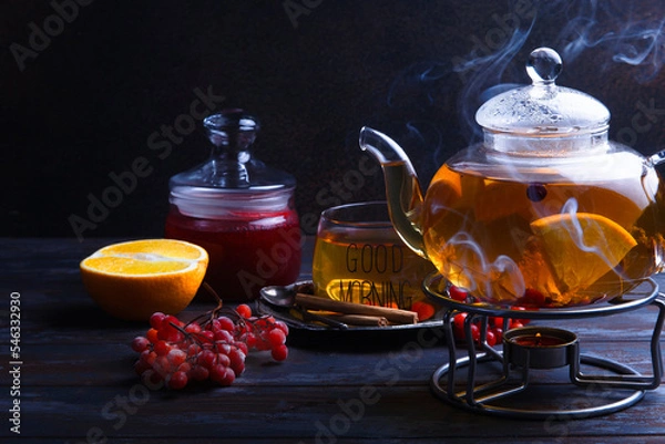 Fototapeta A teapot with hot home made orange and red berries tea with steam, tea time concept.