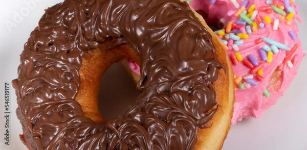 Fototapeta Sweet donuts with chocolate icing and another donuts with pink icing and colorful sprinkles served on a plate. Photo Close-up .