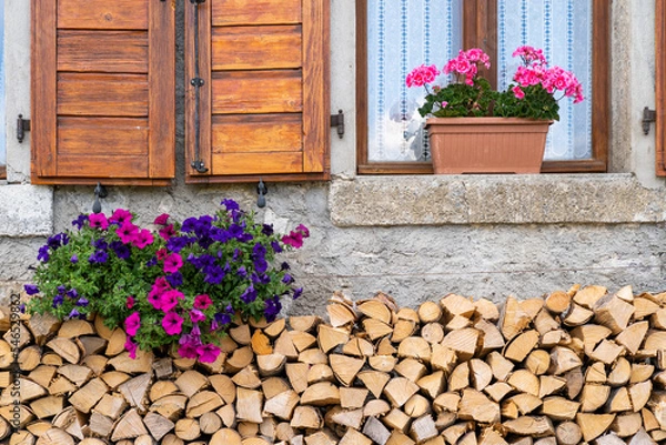 Fototapeta Beautiful cottage window decorated with chopped woods and flowers in a small village in alps, Sauris, Italy