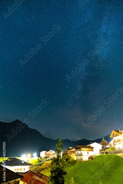 Fototapeta Beautiful night sky with stars and milky way visible above a small village in alps, Sauris, Italy
