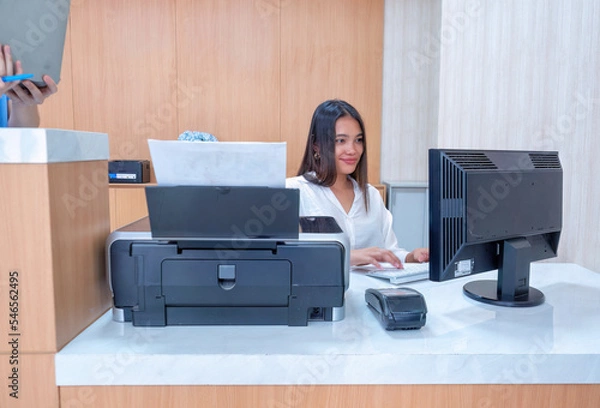 Obraz At hospital hall cashier sit at information counter near receipt printer check patient expense pay