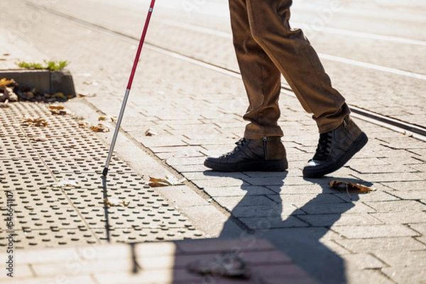 Fototapeta Close-up of a blind man with a walking stick. Detects tactile tiles for self-orientation while moving through the streets of the city