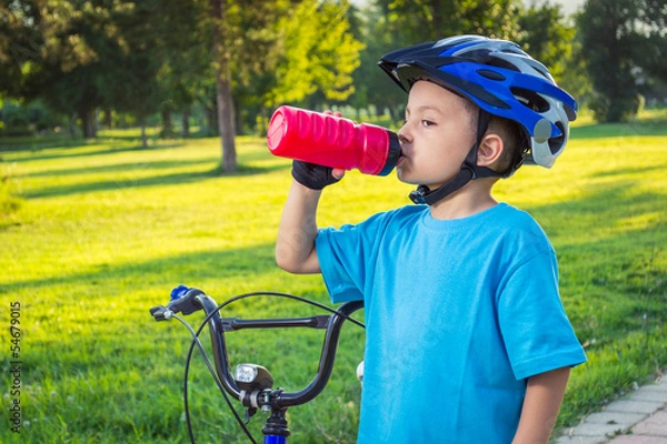 Fototapeta Little boy drinking water by the bike