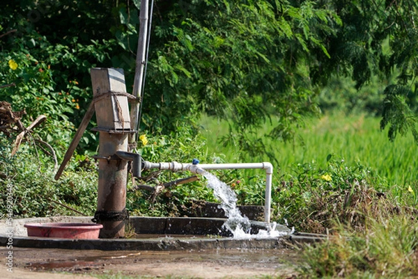 Fototapeta Water flow from pumping pipe and Old hand operated water pumping rural India high water pressure with trees and greenery in background