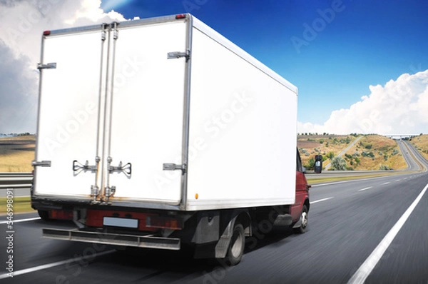 Fototapeta Big white box truck on a road in motion against a sky with clouds