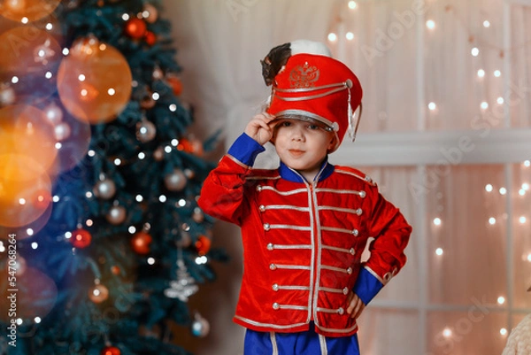 Fototapeta A boy in a nutcracker costume plays with the mouse symbol of the year. christmas tree and gifts