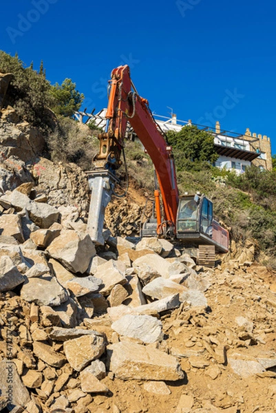 Obraz Heavy organge excavator with shovel standing on hill with rocks