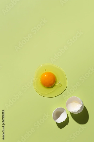 Fototapeta Raw egg yolk on a green background, next to a broken shell. View from above.