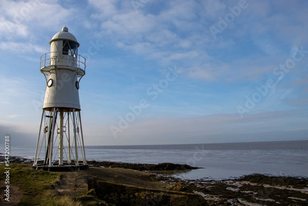 Fototapeta Lighthouse tower by the sea with coast and clouds