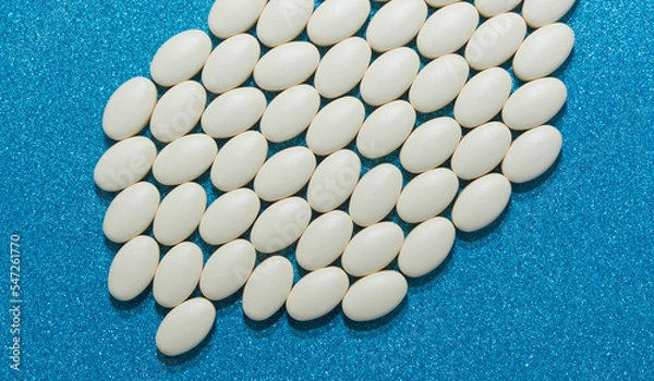 Obraz Large tablets of white color on a blue shiny background. A medicinal product.