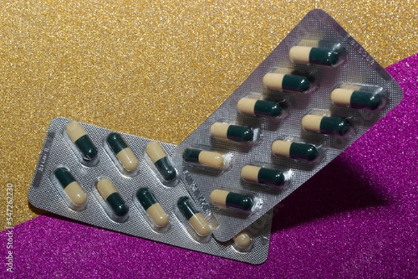 Obraz Капсулы бело-зеленые на розово-желтом фоне. Лекарственный препарат.