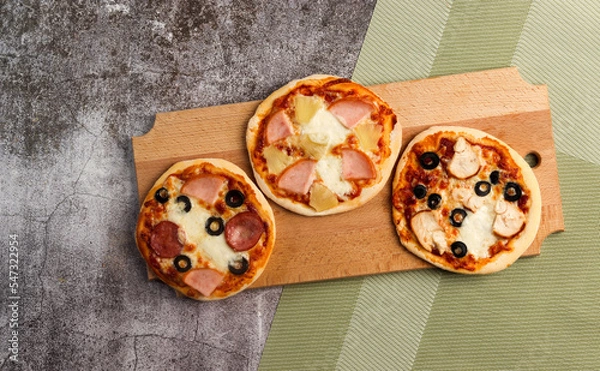 Obraz Pizzette or mini-pizza on a wooden cutting board on a dark grey background. Top view, flat lay