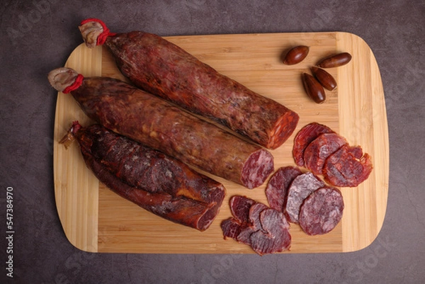 Fototapeta Iberico sausage, Iberico chorizo and Iberico loin on cutting board and dark gray table, garnished with acorns