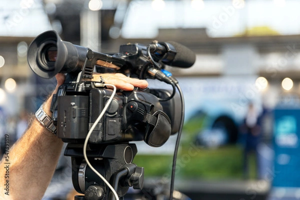 Fototapeta Camera operator filming media event, news or press conference with a professional video camera