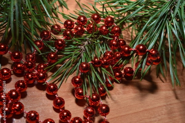 Obraz Shiny red beads on a wooden surface with a pine branch, the celebration of the new year holiday