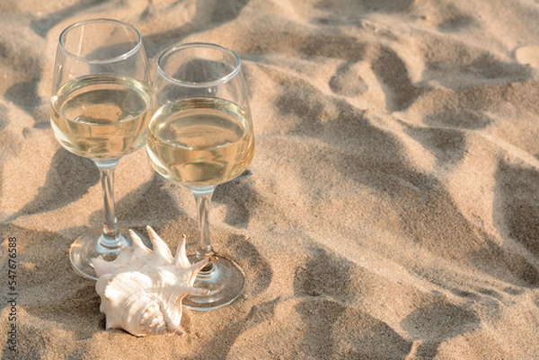 Fototapeta Glasses of tasty wine and seashell on sand, space for text