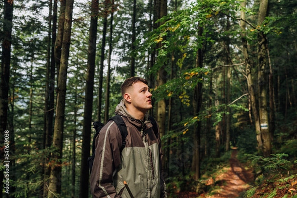 Fototapeta Portrait of a handsome young man in casual clothes standing on a path in the mountains and looking away with a serious face.