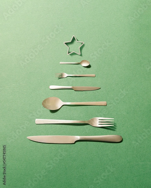 Fototapeta Silver cutlery arranged in the shape of a Christmas tree on a green background. New Year's dinner minimal concept.