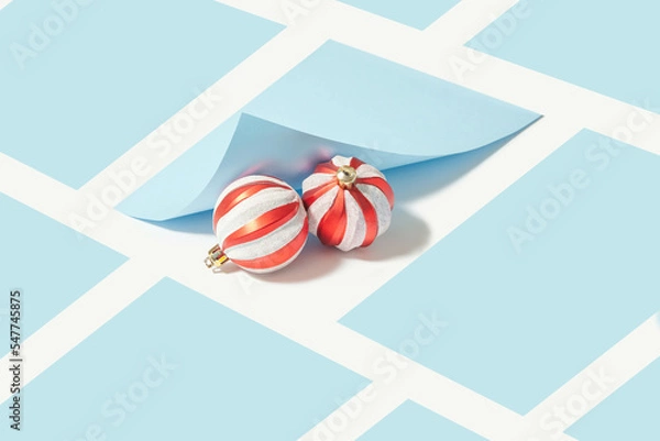 Fototapeta Creative composition with two red Christmas baubles under a pastel blue folded sheet of paper. Geometric background. Minimal xmas holidays concept.