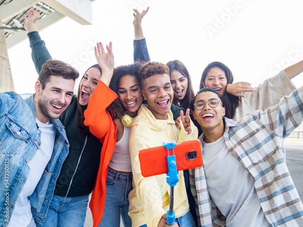 Fototapeta Group of diverse young friends enjoying and laughing in a city taking a selfie