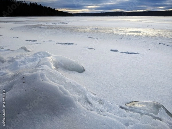 Fototapeta Ice covered in snow on the beach of a lake.