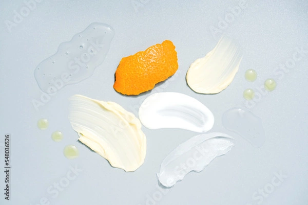 Fototapeta Many cosmetic products samples with vitamin C - cream and gel smears, oil drops over light gray background. Cream smudges texture. Antiaging skincare products with citruc extract and orange peel