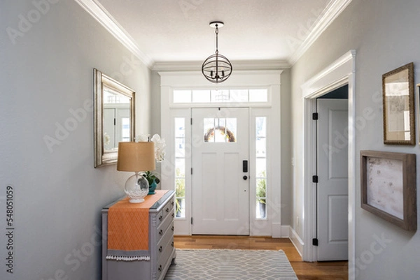 Fototapeta An open large and wide interior front door hallway foyer with transom, hanging light fixture, coastal colors and entry way table and wood floors