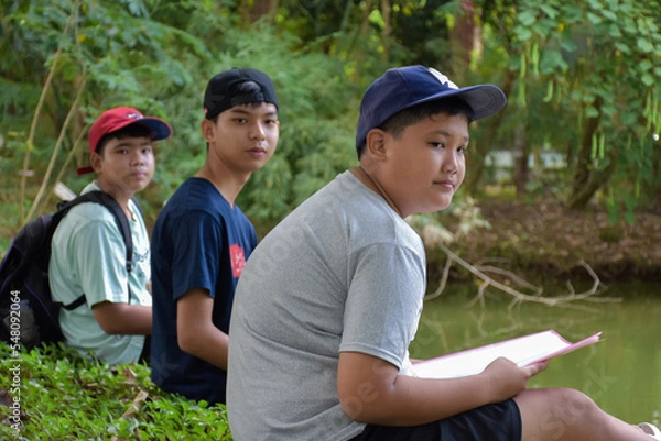 Fototapeta Portrait Asian boys learning the spicies of trees, branches, roots, trunk and information of plants in botanical garden outside the classroom with friends during summer camp, soft focus.