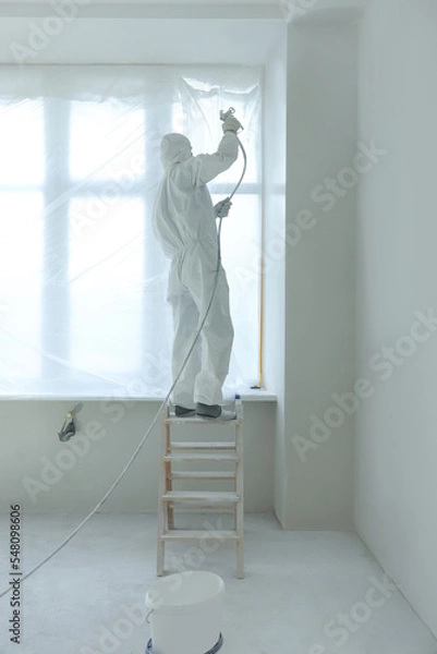 Fototapeta Decorator painting window slope on ladder indoors, back view