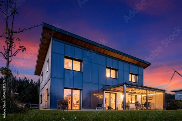 Obraz Illuminated wooden prefabricated house in the evening with a sustainable and self-sufficient energy concept with photovoltaic and solar thermal collectors