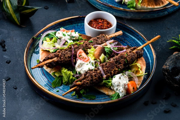 Fototapeta Fresh kebab, barbecued beef on a stick with tomatoes, lettuce, onion, arugula, sour cream, tortilla and red sauce.