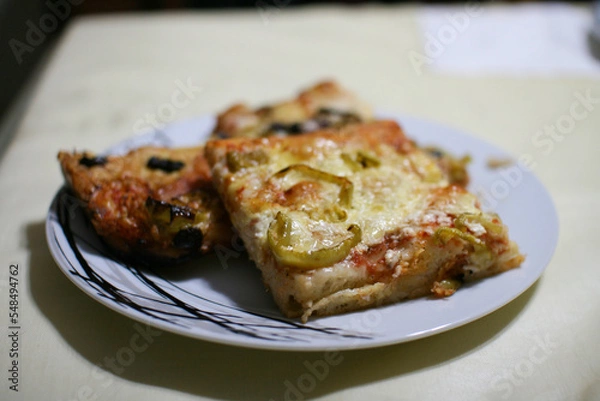Obraz Pieces of homemade italian pizza on a plate closeup, with green peppers, cheese, mushrooms, tomato sauce and olives