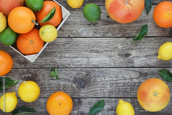 Obraz Citrus fruit decorative frame or border on wooden background. Arranged whole oranges, lemons, limes and grapefruits with leaves on wood board. Top view. Photo from above.