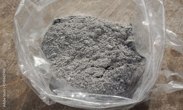 Fototapeta Gray ashes in a plastic bag placed on a wooden floor for use as a fertilizer for plants growing in an agricultural garden.