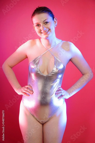 Fototapeta Beautiful cheerful woman posing in silver metallic one piece swimsuit in front of pink background in studio	
