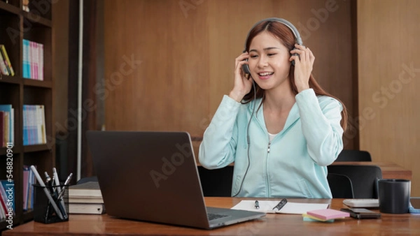 Fototapeta Female student touching headphone and using laptop for studying online learning to preparing for examination