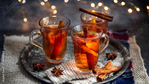 Fototapeta Hot drink for New Year, Christmas or autumn holidays. Mulled cider or spiced punch, tea or mulled white wine with lemon, apples, cinnamon, anise, cloves on a dark background. No People.