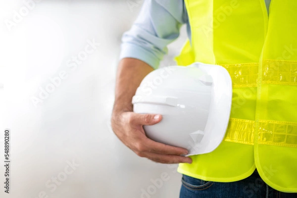 Fototapeta Engineer holding hardhat wearing yellow vest and standing ready for work safety in site.