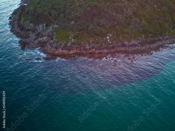 Fototapeta Drone photo looking down at the coastline of Shark Island, Fingal Bay, with contrasting shallow and deep blue water.