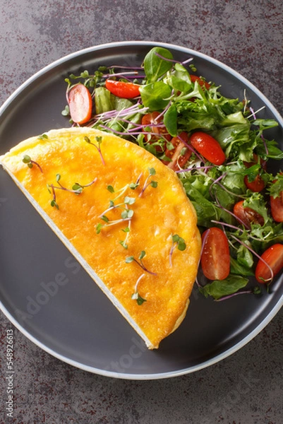 Fototapeta Lunch or dinner egg dishes is the famous Poulard Omelette with vegetables salad closeup on the plate on the dark background. Vertical top view from above