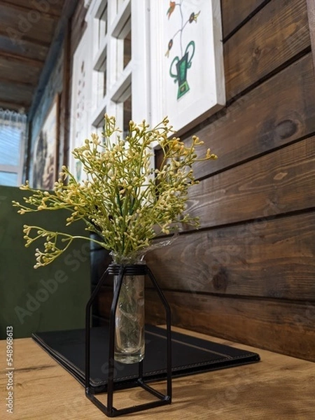 Fototapeta stylish decorative flowers in a modern vase on the table against the background of a wooden wall with a window