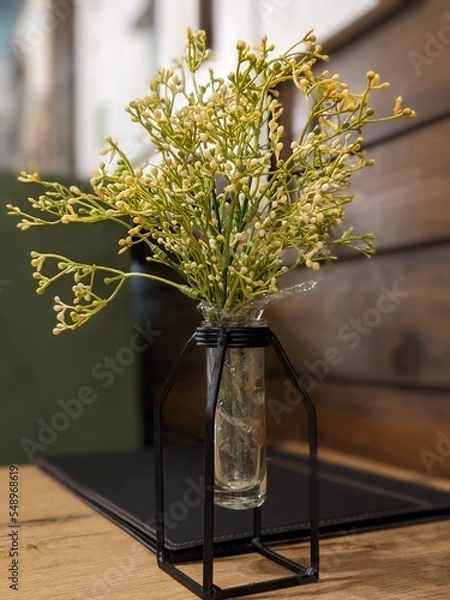 Obraz stylish decorative flowers in a modern vase on the table against the background of a wooden wall with a window