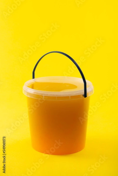 Fototapeta Full transparent bucket with bee honey on a yellow background