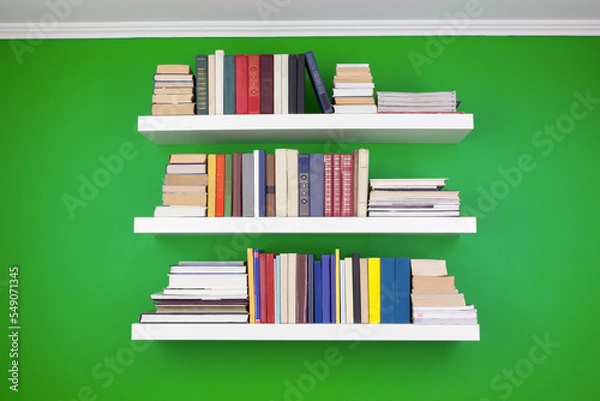 Fototapeta neat stacks and rows of books on white shelves against a green wall