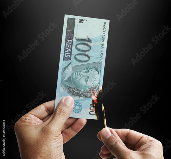 Obraz Burning money. Male hand setting a 100 reais bill on fire. Money from Brazil. 3d rendering.