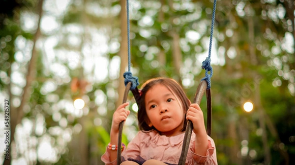 Fototapeta Portrait dreamy funny little girl riding on swing in the twilight with nature background