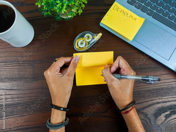 Fototapeta women write in yellow notes, mock up yellow notes. Women's hands write notes on yellow note paper in the background of the office desk workspace from the top view.